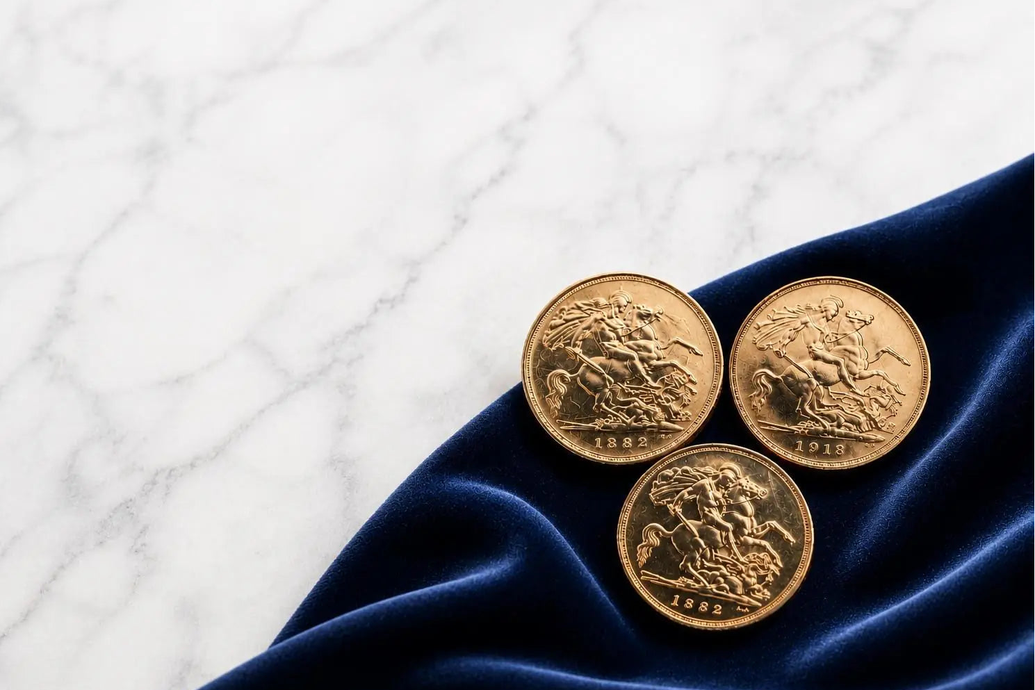 Three gold sovereign coins on a blue fabric with a white marble textured background | 999 Bullion